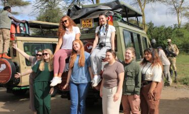 Group of safari travelers posing beside Bush Doctor Safaris 4x4 vehicles in Kenya.