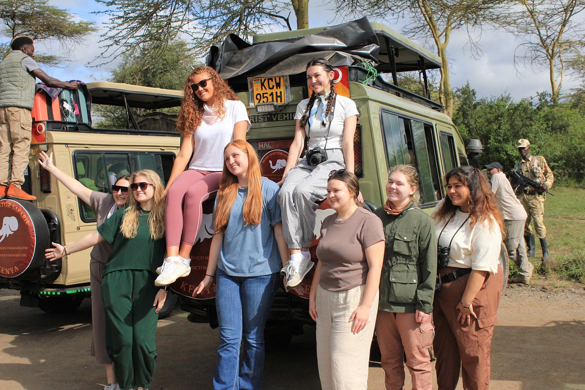 Group of safari travelers posing beside Bush Doctor Safaris 4x4 vehicles in Kenya.
